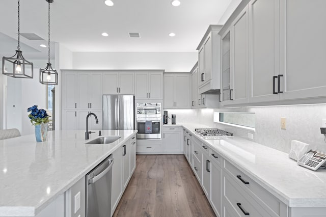 kitchen with light stone countertops, sink, light hardwood / wood-style flooring, a spacious island, and appliances with stainless steel finishes