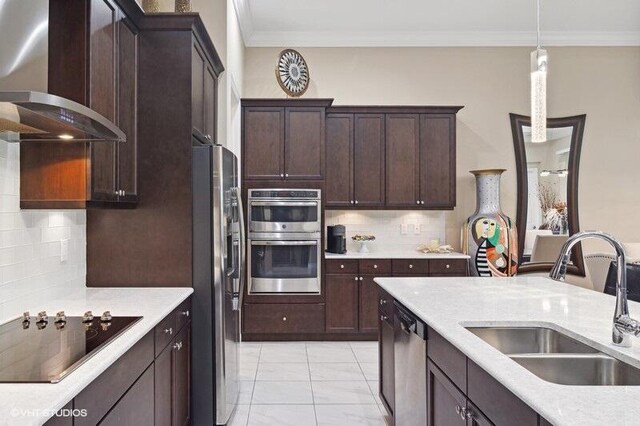 kitchen with light tile patterned flooring, sink, appliances with stainless steel finishes, wall chimney exhaust hood, and decorative light fixtures