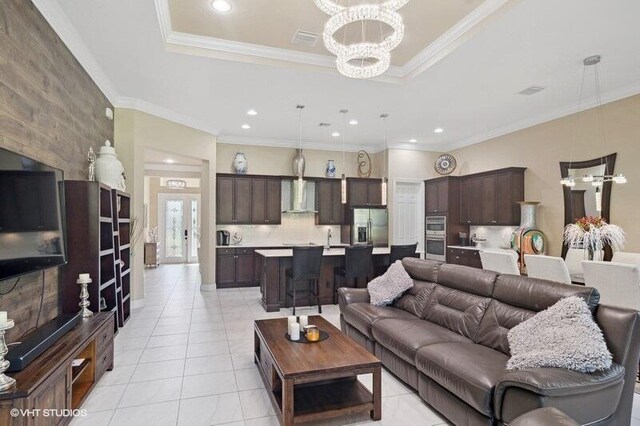 kitchen with hanging light fixtures, sink, a kitchen island with sink, and a tray ceiling