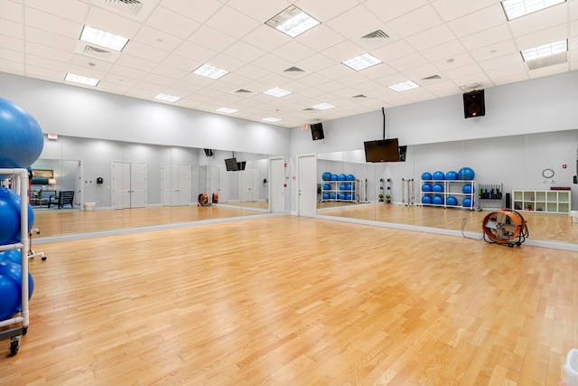 workout area with light hardwood / wood-style floors, a paneled ceiling, and a high ceiling