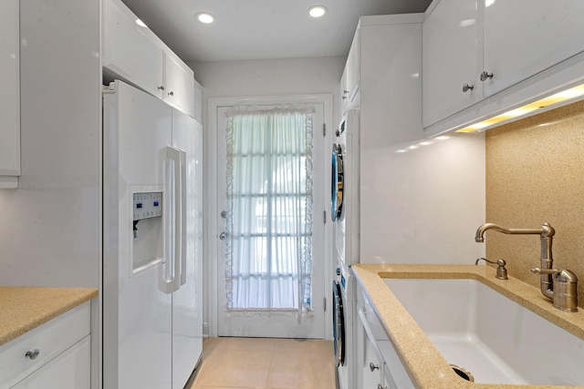 kitchen with stacked washer / dryer, sink, white cabinets, and white fridge with ice dispenser