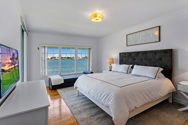 bedroom featuring hardwood / wood-style floors, crown molding, and a water view