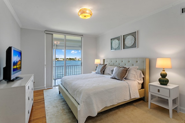 bedroom with a water view, crown molding, light hardwood / wood-style flooring, and access to exterior