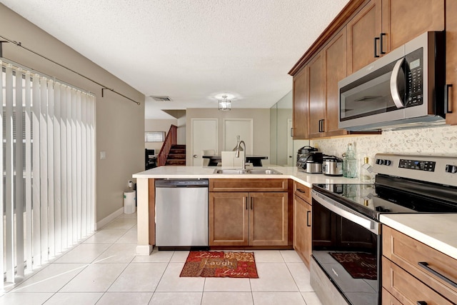 kitchen featuring sink, a textured ceiling, appliances with stainless steel finishes, light tile patterned flooring, and kitchen peninsula