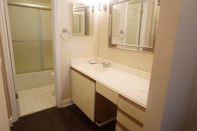 full bathroom featuring hardwood / wood-style floors, enclosed tub / shower combo, vanity, and toilet