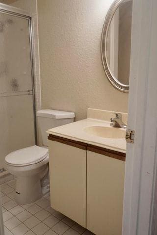 bathroom featuring toilet, vanity, tile patterned flooring, and a shower with shower door