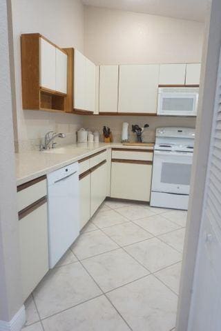 kitchen with white appliances, sink, light tile patterned floors, and white cabinets