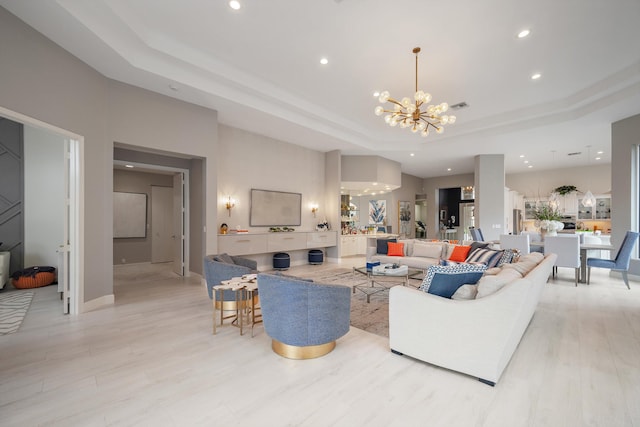 living room with light hardwood / wood-style flooring, a tray ceiling, and an inviting chandelier