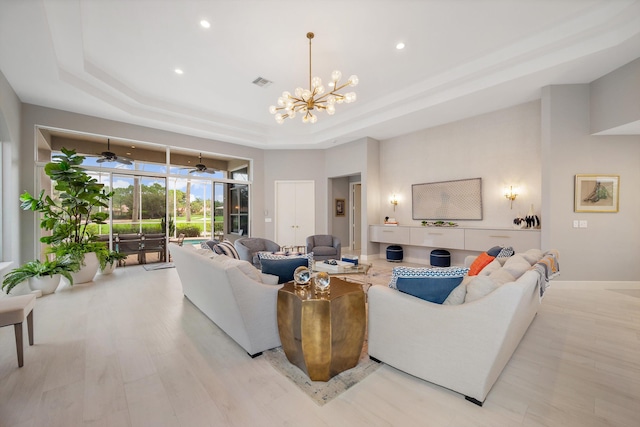 living room with light hardwood / wood-style flooring, a tray ceiling, and ceiling fan with notable chandelier