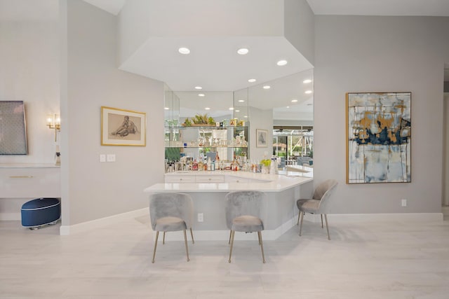 kitchen with white cabinetry, a kitchen bar, a towering ceiling, and kitchen peninsula