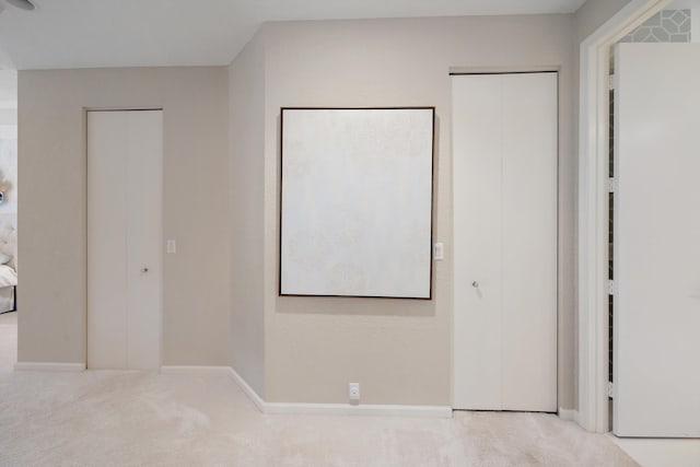 unfurnished bedroom with multiple closets and light colored carpet