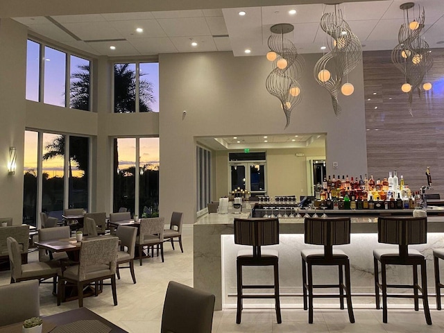 bar with light stone counters, a towering ceiling, light tile patterned flooring, and hanging light fixtures