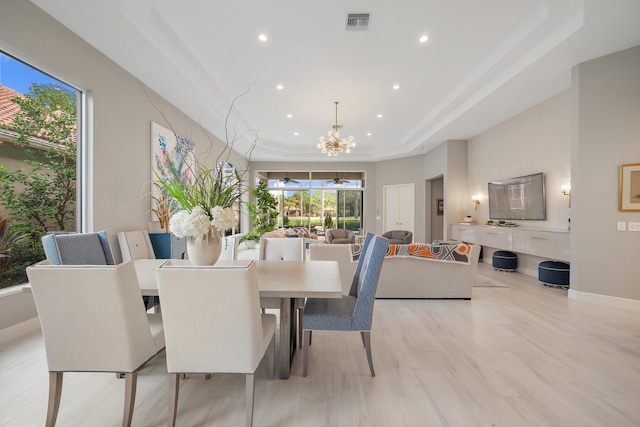 dining area with a notable chandelier, light wood-type flooring, and a raised ceiling