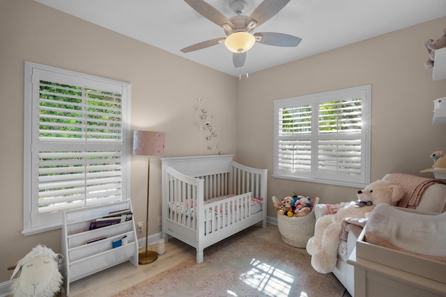 bedroom featuring ceiling fan, light hardwood / wood-style flooring, and a crib