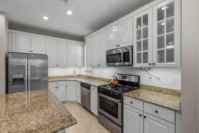 kitchen with tasteful backsplash, appliances with stainless steel finishes, white cabinetry, dark stone countertops, and light tile patterned floors