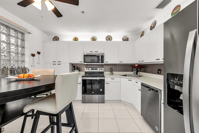 kitchen with appliances with stainless steel finishes, white cabinetry, a textured ceiling, and light tile patterned floors