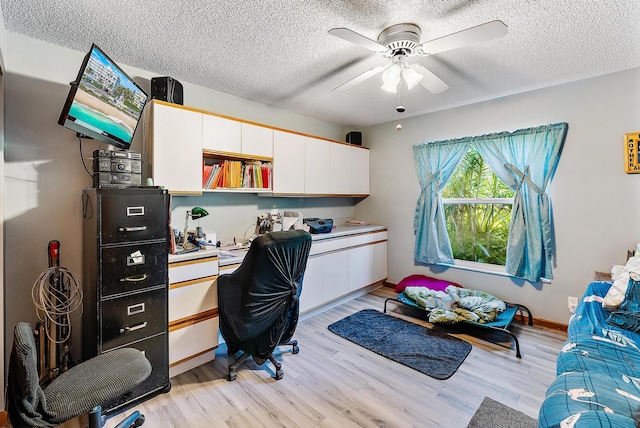 home office featuring built in desk, ceiling fan, a textured ceiling, and light wood-type flooring