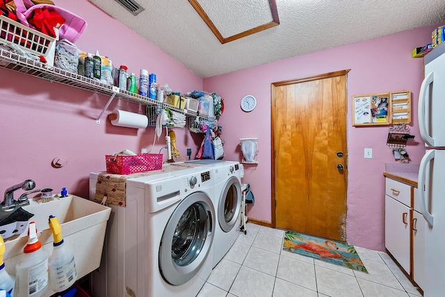 clothes washing area with a textured ceiling, sink, washer and clothes dryer, and light tile patterned floors