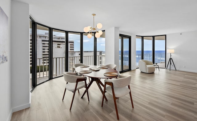 dining room with a chandelier, a water view, light hardwood / wood-style floors, and a wall of windows