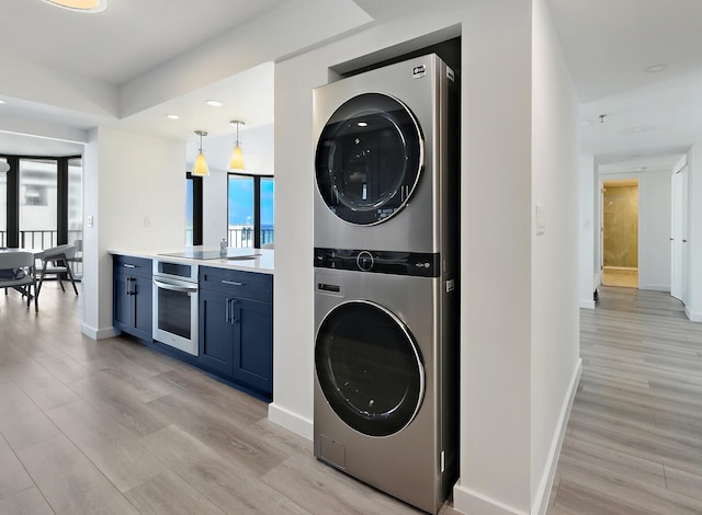 clothes washing area with stacked washer / dryer and light hardwood / wood-style flooring