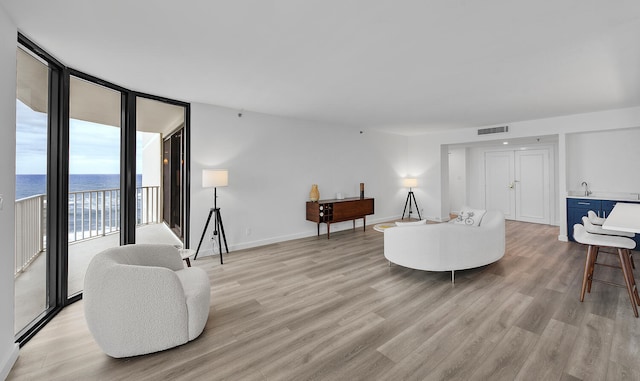 living room with floor to ceiling windows, a water view, sink, and light hardwood / wood-style floors