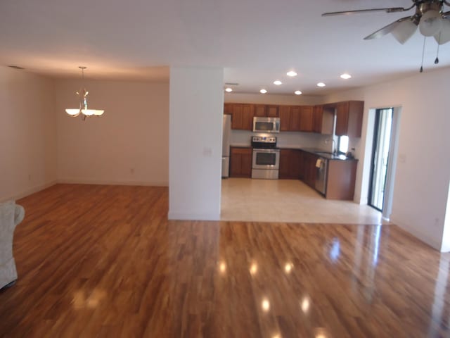 kitchen featuring stainless steel appliances, sink, ceiling fan with notable chandelier, hanging light fixtures, and light wood-type flooring