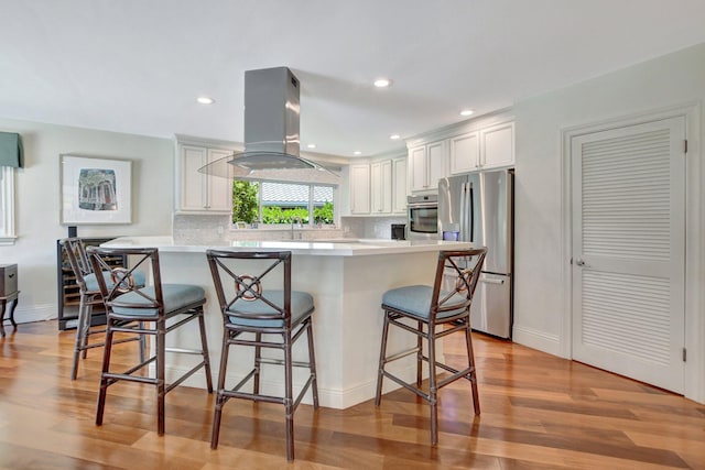 kitchen featuring island range hood, a kitchen breakfast bar, stainless steel appliances, white cabinets, and light hardwood / wood-style floors