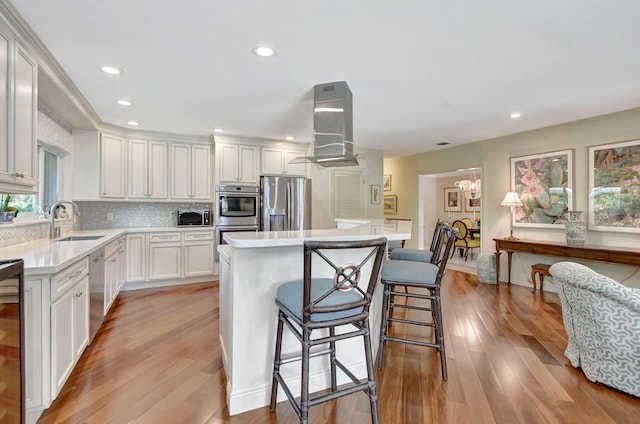 kitchen featuring white cabinets, a kitchen island, appliances with stainless steel finishes, light wood-type flooring, and island range hood