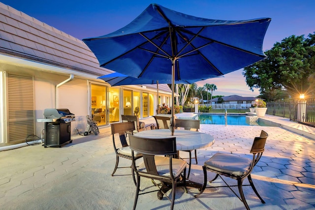 pool at dusk with a patio area and a grill