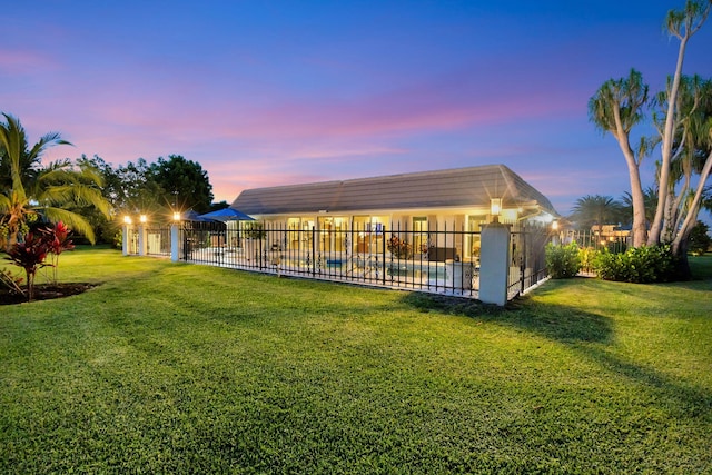 back house at dusk featuring a lawn