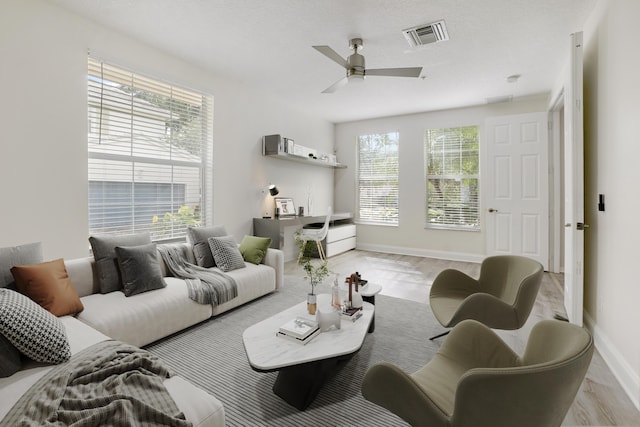 living room with baseboards, visible vents, ceiling fan, light wood-style flooring, and a textured ceiling