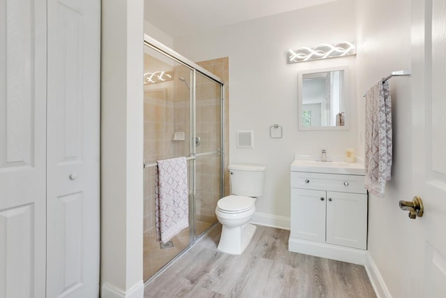 bathroom with toilet, wood finished floors, vanity, a closet, and a shower stall