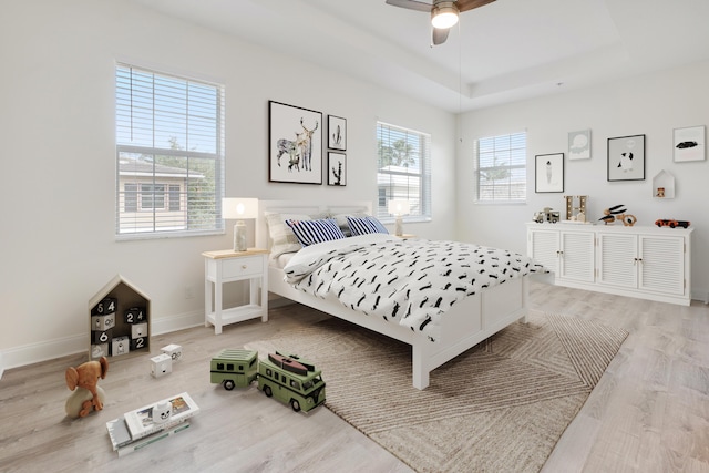 bedroom featuring a tray ceiling, ceiling fan, light wood-style flooring, and baseboards