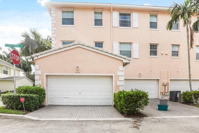 townhome / multi-family property with central AC, an attached garage, and stucco siding