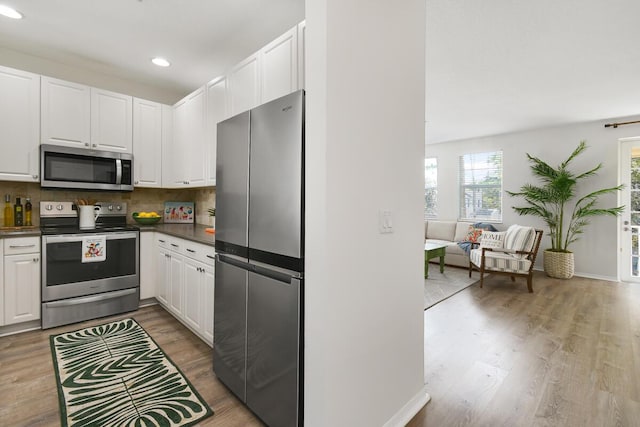 kitchen with appliances with stainless steel finishes, dark countertops, white cabinets, and light wood-style flooring