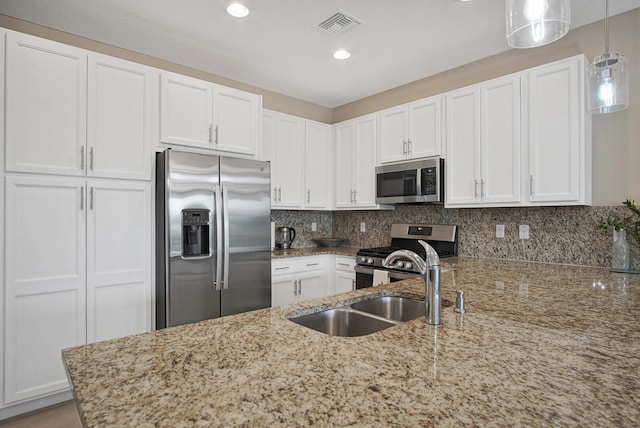 kitchen with light stone counters, appliances with stainless steel finishes, pendant lighting, and white cabinets