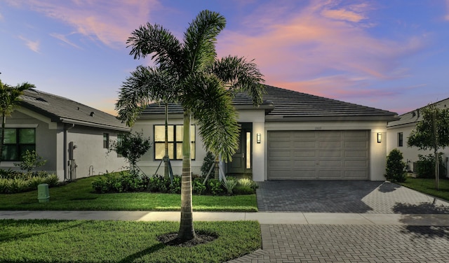 ranch-style home with decorative driveway, a garage, stucco siding, and a front yard
