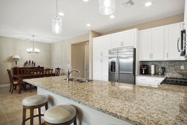 kitchen with hanging light fixtures, stainless steel appliances, sink, light stone countertops, and white cabinets