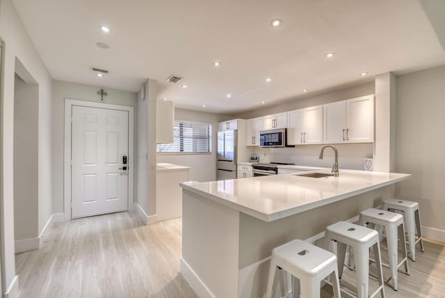 kitchen with kitchen peninsula, appliances with stainless steel finishes, sink, white cabinets, and a breakfast bar area