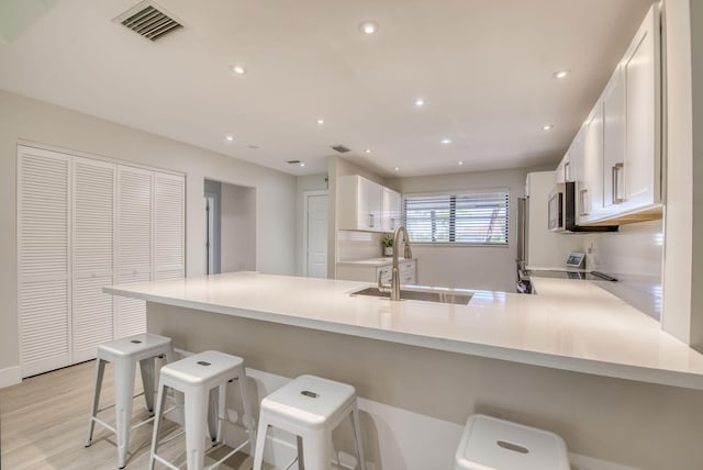 kitchen featuring kitchen peninsula, appliances with stainless steel finishes, a breakfast bar, sink, and white cabinets