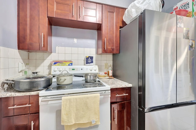 kitchen with decorative backsplash, electric range, light stone counters, and stainless steel refrigerator