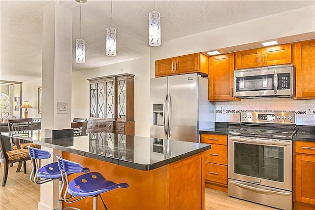 kitchen featuring a center island, a kitchen breakfast bar, stainless steel appliances, pendant lighting, and light hardwood / wood-style flooring