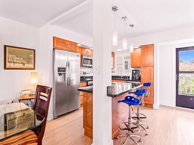 kitchen with sink, a kitchen bar, pendant lighting, appliances with stainless steel finishes, and light hardwood / wood-style floors