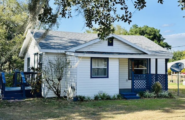 view of front of house with covered porch, a shingled roof, and a front yard