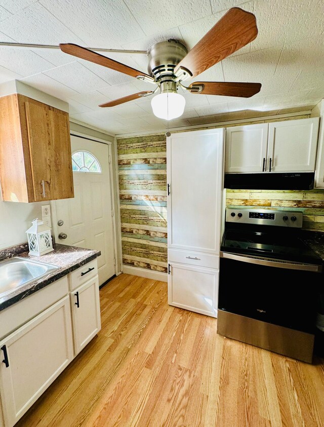 kitchen with light wood finished floors, extractor fan, stainless steel range with electric cooktop, white cabinetry, and a sink