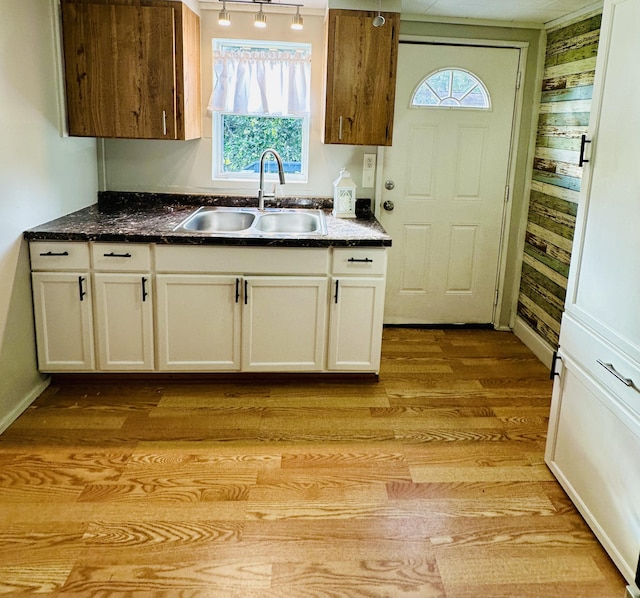 kitchen featuring white cabinetry, a sink, wood walls, and light wood finished floors