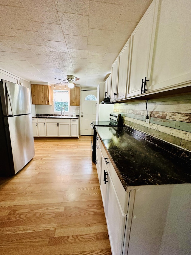 kitchen with dark countertops, light wood-style flooring, ceiling fan, appliances with stainless steel finishes, and a sink