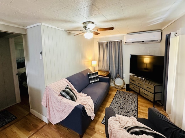 living area with a ceiling fan, an AC wall unit, and wood finished floors