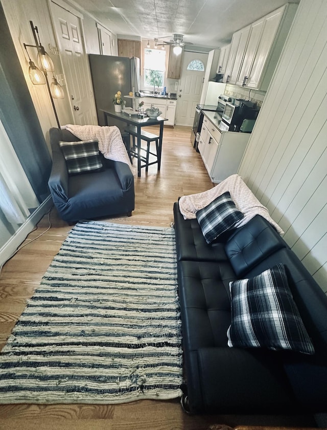 living area featuring light wood-type flooring, a ceiling fan, and wood walls