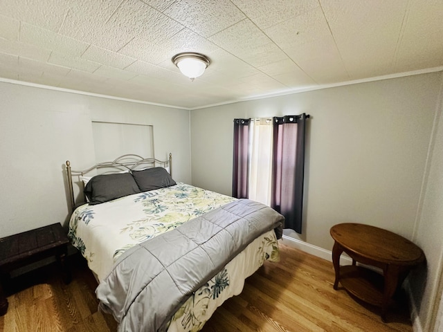 bedroom with wood finished floors and ornamental molding
